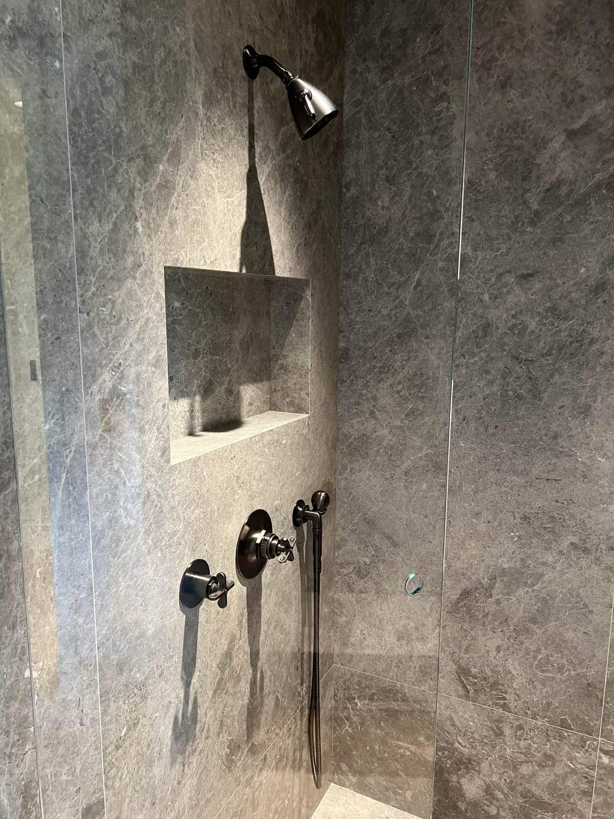 Finished shower in gray marble with a recessed niche, hand shower, and dark bronze valve trim