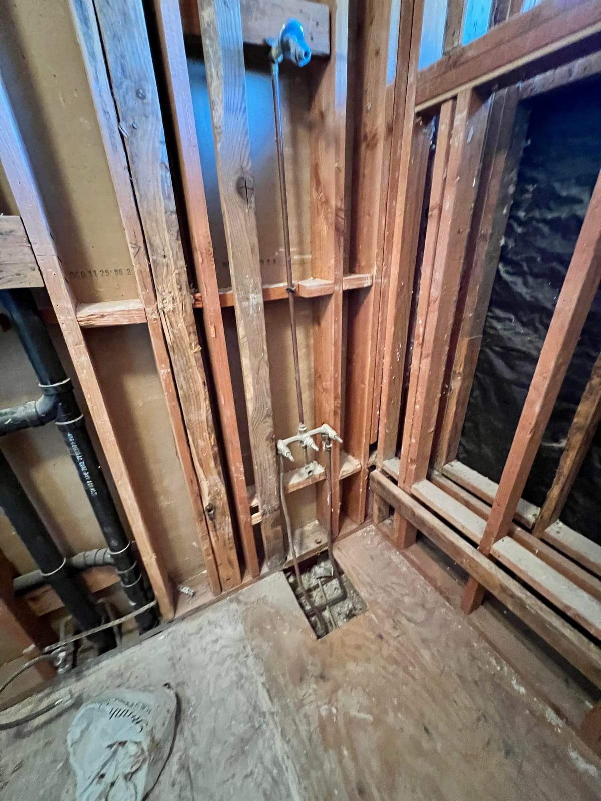 Shower stripped to the studs, with the valve roughed in and a bench framed along one wall