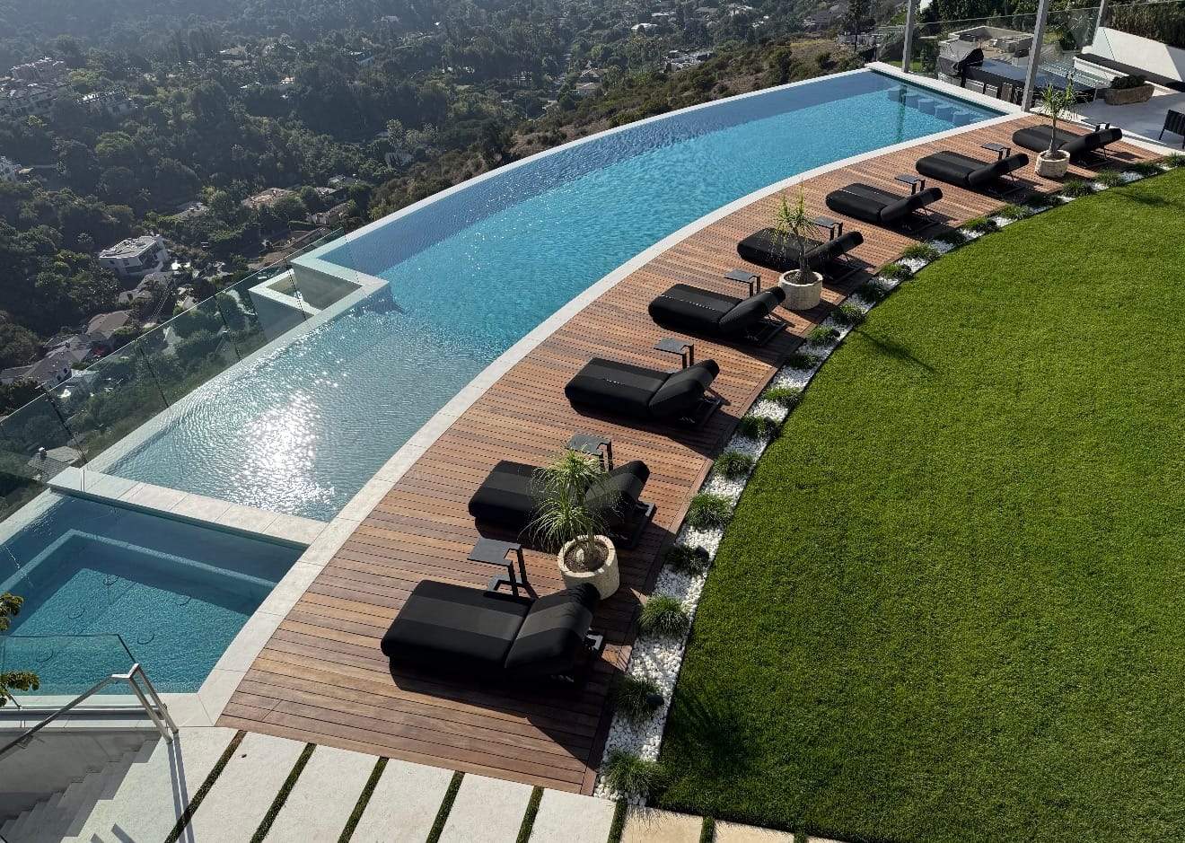 Finished curved infinity pool with an ipe deck, lounge chairs, and city views