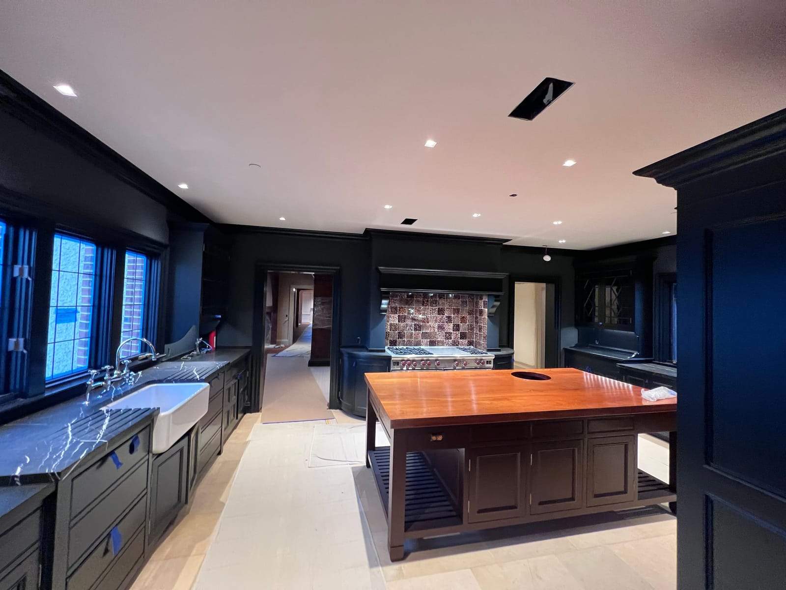 Dark-painted kitchen with a farmhouse sink, marble counters, and a butcher-block island