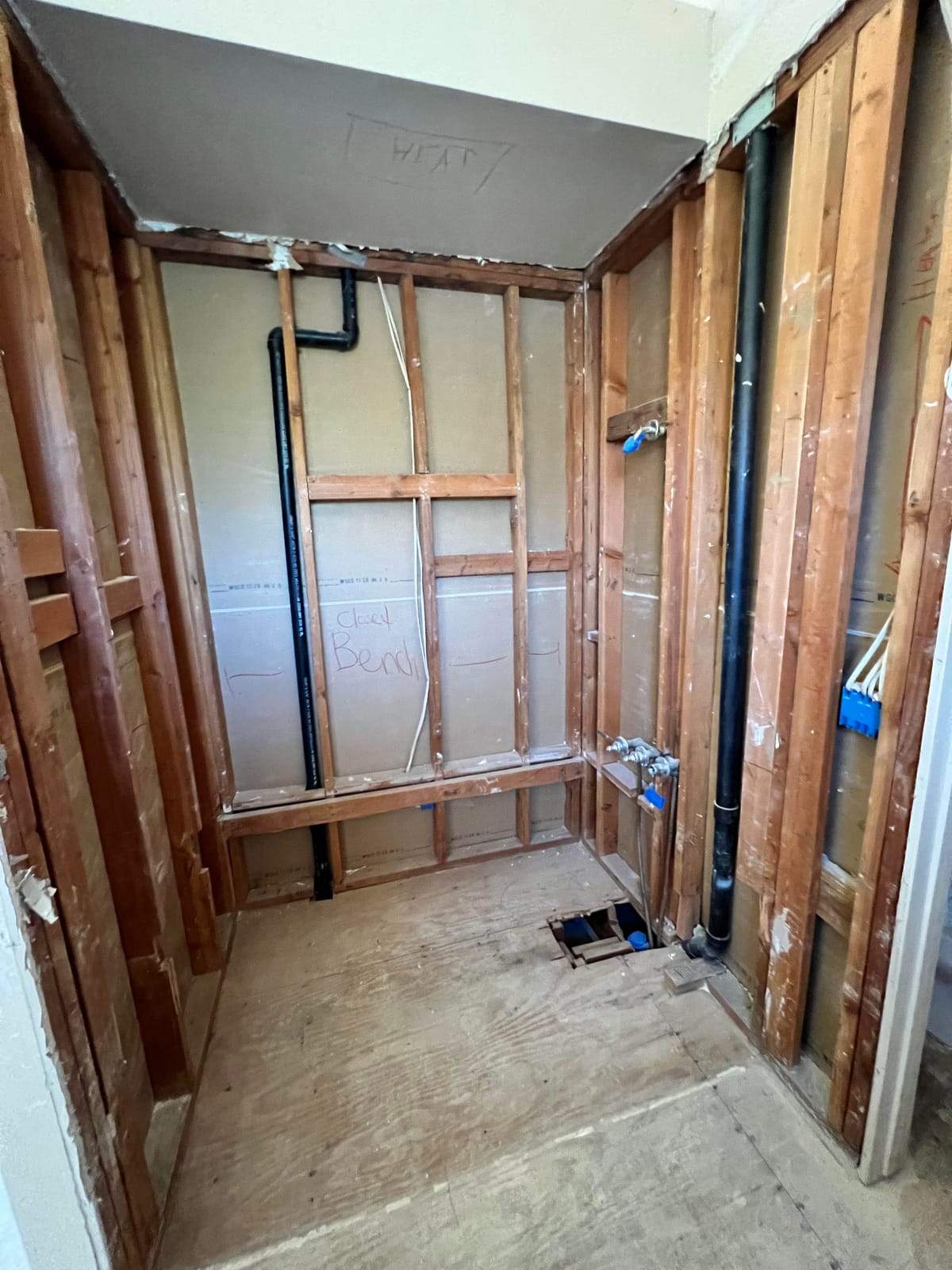 Shower opened to the studs, with new drain lines and a framed bench